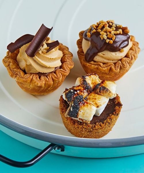 Three mini dessert cups: one with chocolate curls, one with chocolate frosting and nuts, and one with toasted marshmallows.