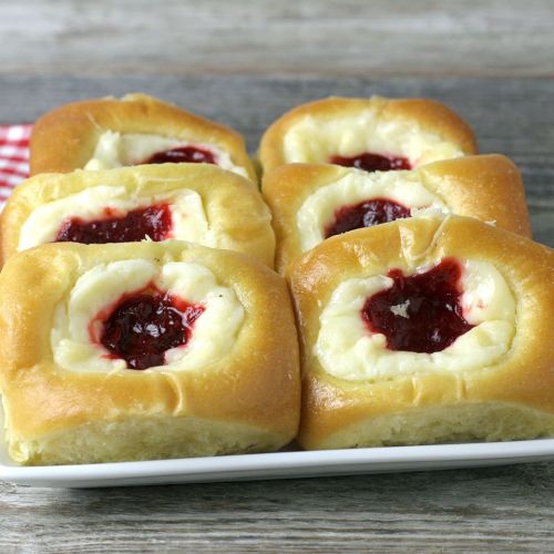 A plate of six sweet rolls filled with cream cheese and raspberry jam, arranged neatly on a wooden surface.