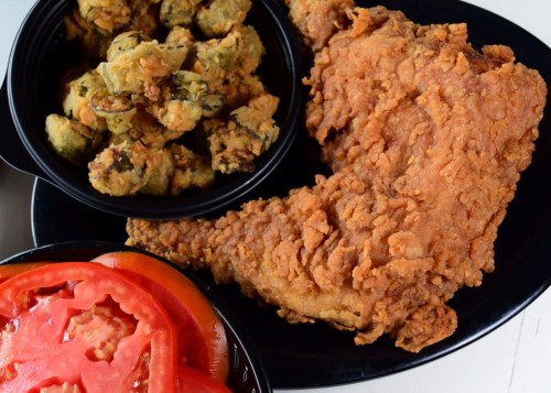 A plate featuring a large piece of fried chicken, a side of fried okra, and fresh tomato slices.