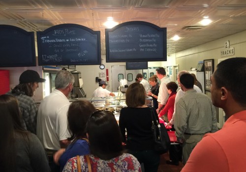A crowd of people waits in line at a restaurant counter with a menu displayed above.