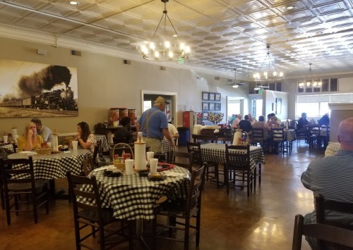 A cozy restaurant interior with checkered tablecloths, diners enjoying meals, and vintage train decor on the wall.