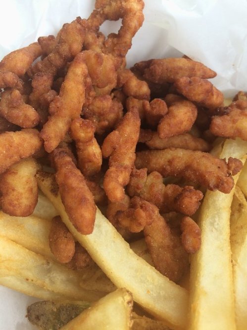 A close-up of crispy fried chicken pieces mixed with golden French fries in a takeout container.