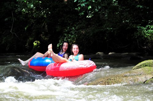 Two girls float on colorful inner tubes in a river, enjoying a sunny day surrounded by greenery.