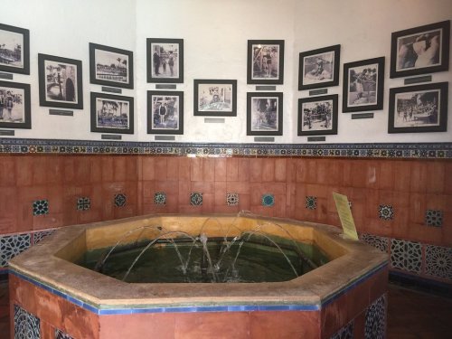A decorative octagonal fountain in a room adorned with historical black-and-white photographs on the walls.