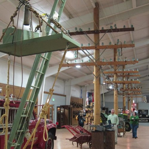 A museum exhibit featuring vintage utility poles, glass insulators, and old vehicles in a spacious indoor setting.