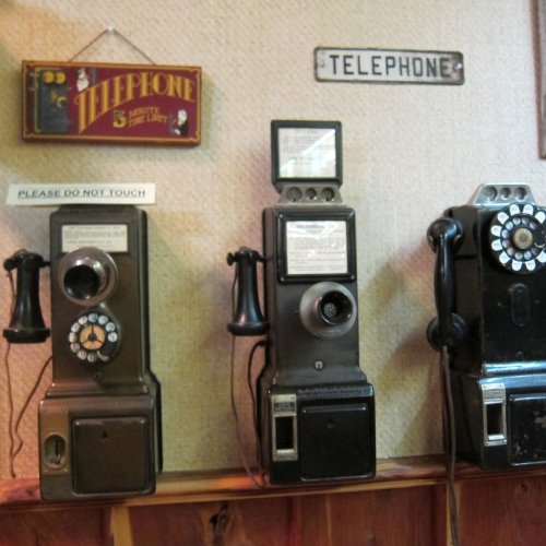 Three vintage payphones mounted on a wall, with signs reading "PLEASE DO NOT TOUCH" and "TELEPHONE."