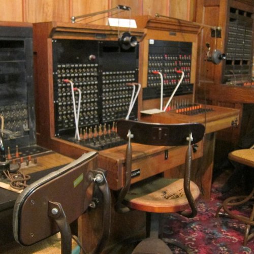 Vintage telephone switchboard with multiple connections and a wooden chair in a retro setting.