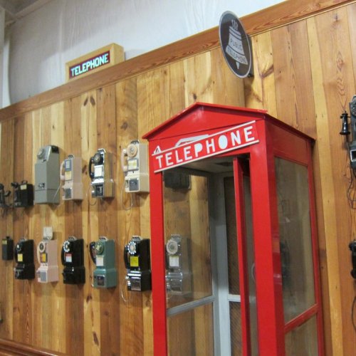 A vintage red telephone booth next to various old-fashioned telephones on a wooden wall.