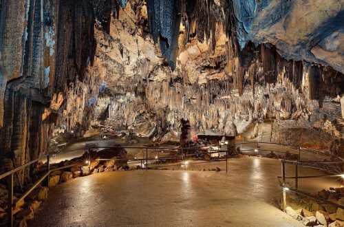 A stunning cave interior with stalactites and stalagmites, illuminated by soft lights along a stone pathway.