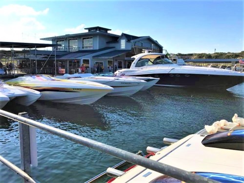 A marina scene with several boats docked near a waterfront building under a clear blue sky.