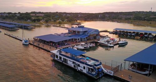 Aerial view of a marina at sunset, featuring boats docked and a blue-roofed building along the water.
