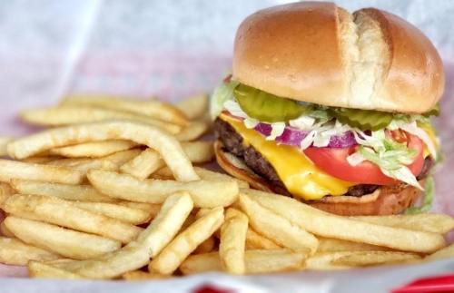 A juicy cheeseburger with lettuce, tomato, pickles, and onions, served with a side of golden French fries.