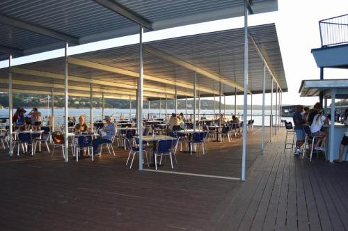 A spacious outdoor dining area with tables and chairs, overlooking a body of water at sunset.