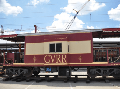 A vintage railroad car with "GVRR" on the side, parked under a blue sky with cranes in the background.