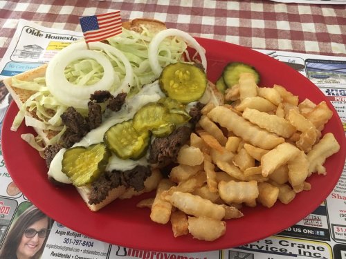 A plate of a sandwich with beef, pickles, onions, and lettuce, served with a side of crinkle-cut fries and a small flag.