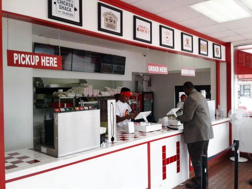 A man in a suit orders at a fast-food counter with signs for pickup and ordering at a chicken restaurant.
