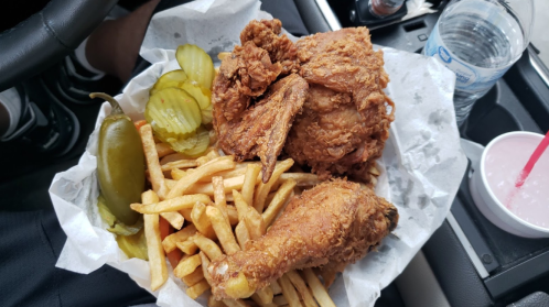 A basket of fried chicken, pickles, jalapeños, and French fries, placed in a car. A water bottle and drink are nearby.