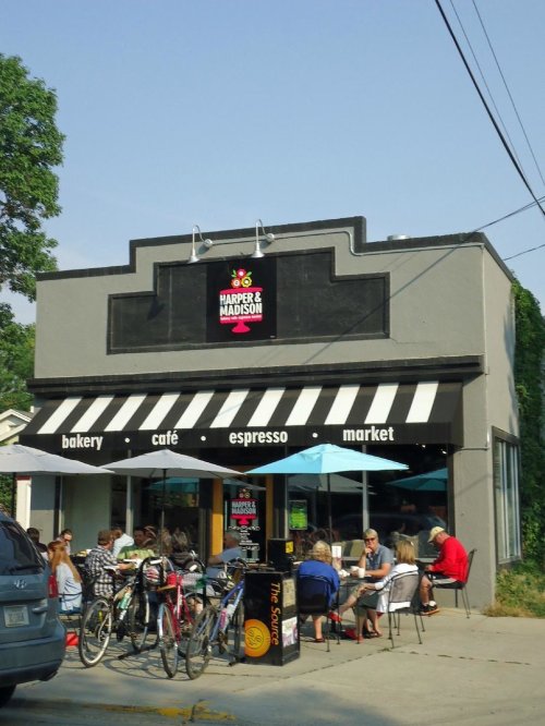 A bakery and café with outdoor seating, people dining, and bicycles parked outside under a striped awning.