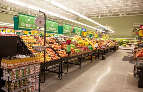 A grocery store aisle filled with colorful organic fruits and vegetables, with scales and signage visible.