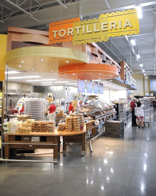 A bustling tortilleria with staff preparing tortillas and baked goods in a bright, inviting store setting.