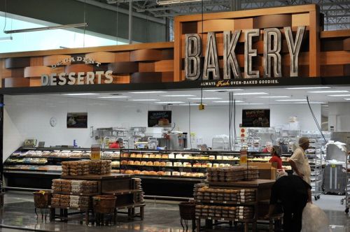 A bakery section in a grocery store featuring fresh baked goods and desserts, with staff and customers browsing.