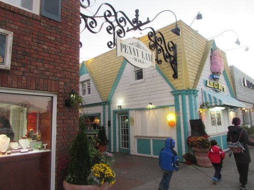 A colorful building with a sign reading "Penny Lane Mall," surrounded by flowers and people walking by.