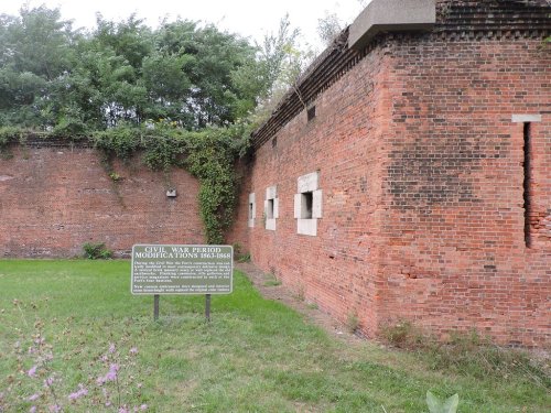 Brick wall of a historic structure with windows, surrounded by greenery and a sign about Civil War modifications.