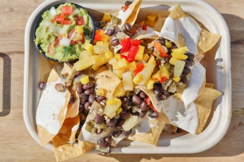 A tray of nachos topped with black beans, diced pineapple, tomatoes, and a side of guacamole.