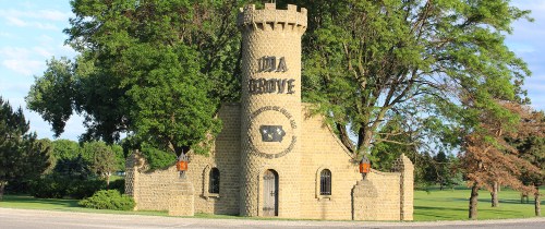 A stone tower with a castle-like design, surrounded by trees and grass, featuring the words "Lida Grove."