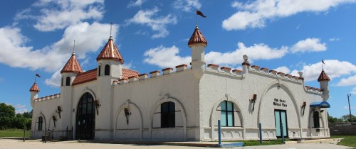 A whimsical building with turrets and a red-tiled roof, set against a blue sky with fluffy clouds.