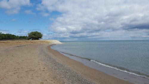 A serene beach scene with sandy shore, pebbles, calm water, and a cloudy sky in the background.
