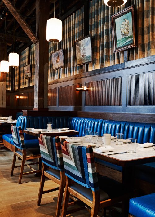 A cozy restaurant interior featuring blue booths, striped chairs, and nautical-themed artwork on the walls.