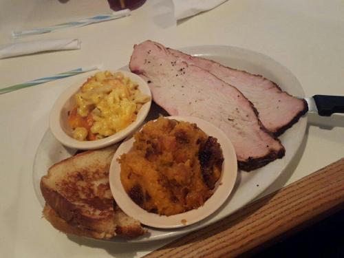 A plate with sliced smoked meat, macaroni and cheese, and sweet potato casserole, alongside a piece of toasted bread.