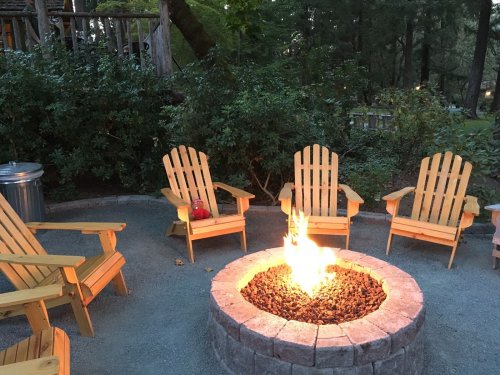A cozy outdoor fire pit surrounded by wooden chairs, set in a lush, green garden.