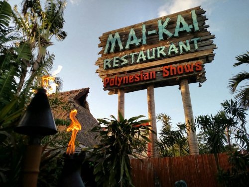 Sign for Mai-Kai Restaurant featuring Polynesian shows, surrounded by tropical plants and tiki torches.