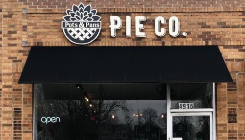 Sign for "Pots & Pans Pie Co." on a brick storefront, featuring an open sign in the window.