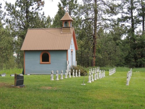 A small, colorful chapel beside a grassy area with white statues arranged in a row, surrounded by trees.