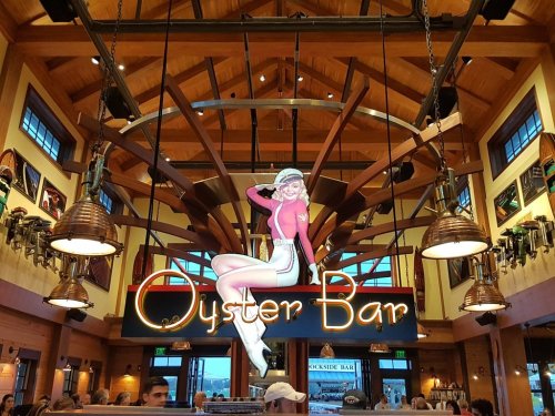 Interior of an Oyster Bar featuring a large sign and a vintage-style woman illustration, with wooden beams and warm lighting.