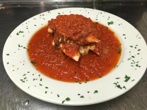 A plate of lasagna topped with marinara sauce and garnished with parsley, served in a rich red sauce.