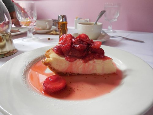 A slice of cheesecake topped with fresh strawberries and a strawberry sauce, served on a white plate.