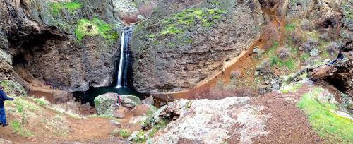 A panoramic view of a waterfall surrounded by rocky cliffs and greenery, with people exploring the area.