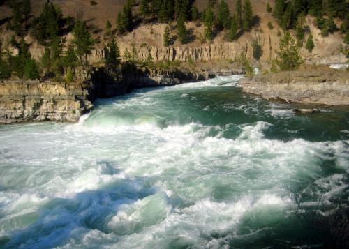 A rushing river flows through rocky cliffs, surrounded by trees and a serene landscape.