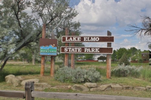 Sign for Lake Elmo State Park in Montana, featuring wooden posts and a blue park logo against a cloudy sky.