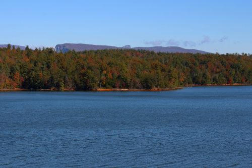 A serene lake surrounded by colorful autumn trees and distant mountains under a clear blue sky.