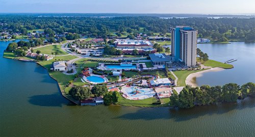 Aerial view of a resort with a water park, hotel, and surrounding greenery by a lake.
