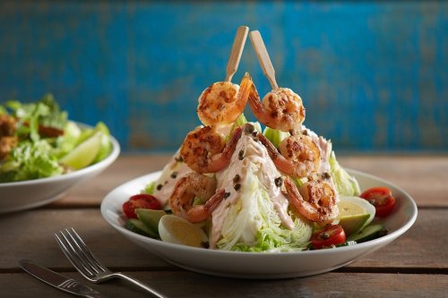 A vibrant salad topped with grilled shrimp, cherry tomatoes, and lime, served on a wooden table.