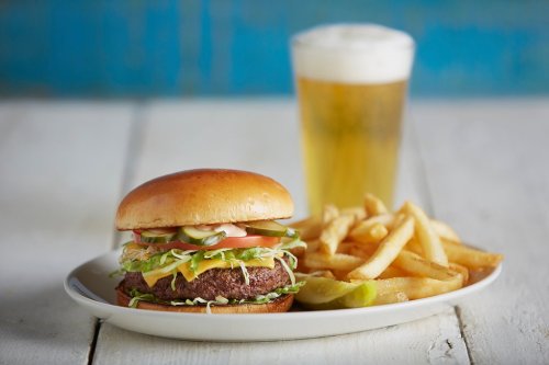 A juicy hamburger with lettuce, tomato, and cheese, served with fries and a glass of beer in the background.