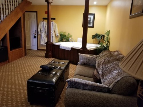 Cozy room with a sofa, ottoman, and a hot tub, featuring warm yellow walls and decorative plants.
