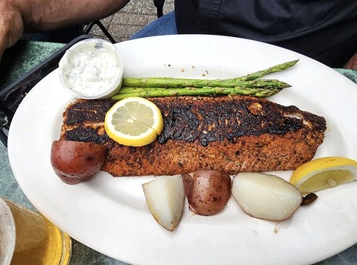 A plate with blackened salmon, lemon slices, asparagus, and roasted potatoes, served with a side of sauce.
