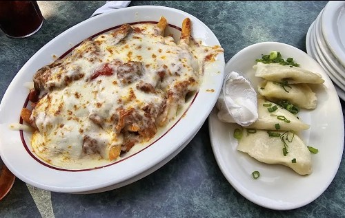 A plate of cheesy fries topped with meat sauce, alongside a dish of dumplings with sour cream and green onions.